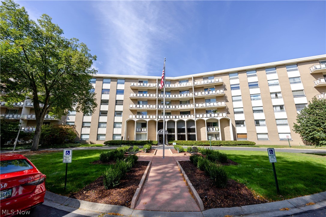 Multi-story condominium with curved balconies, landscaped entrance path, and American flag.