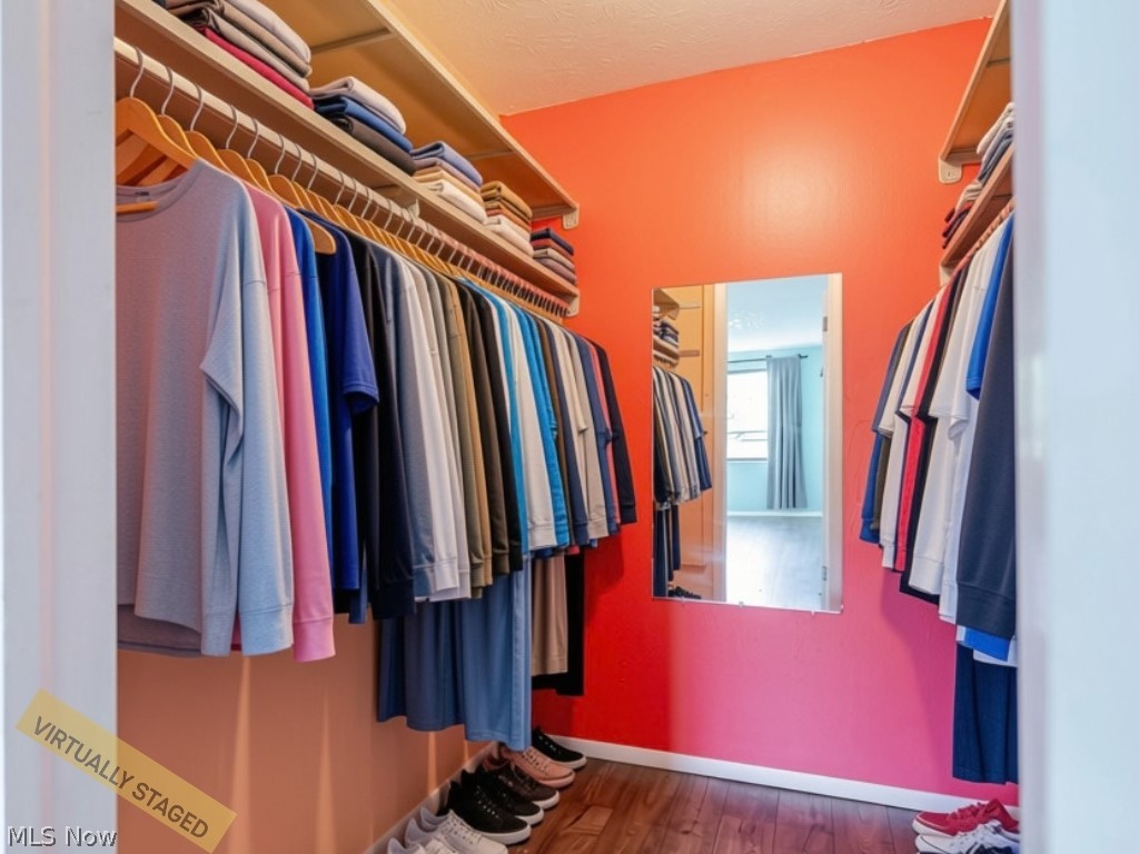 Walk-in closet with clothing on open shelves, a wall mirror, and vivid coral walls.