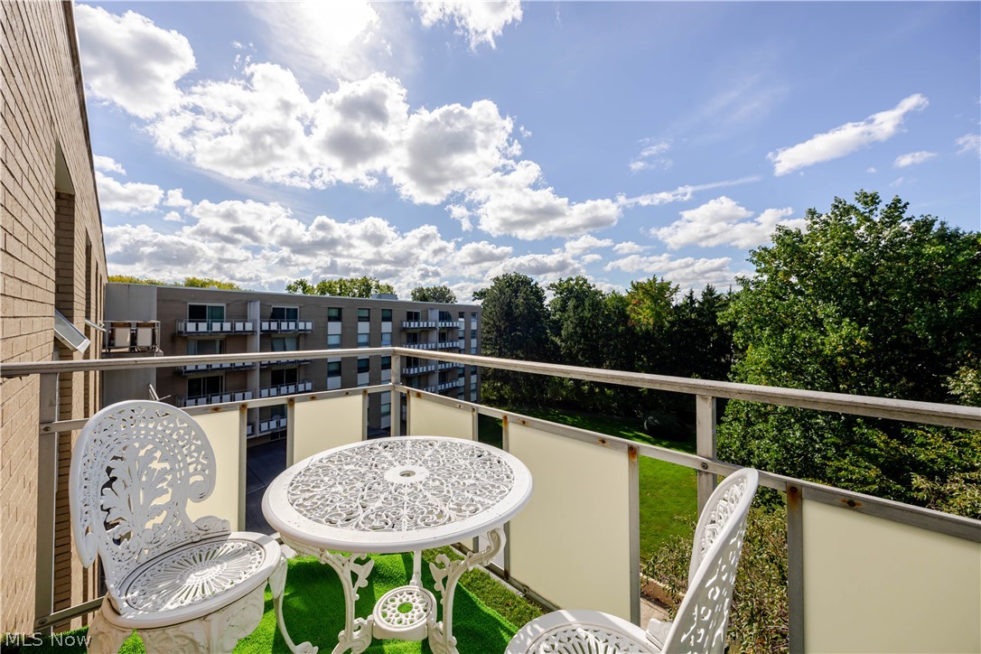 Balcony with ornate white patio furniture overlooking trees and a neighboring apartment building.
