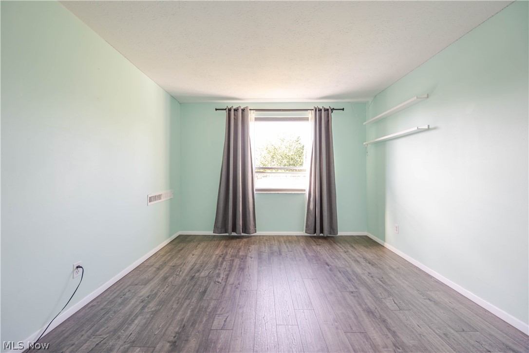 Vacant bedroom with gray wood-look flooring, mint walls, and a curtained window.
