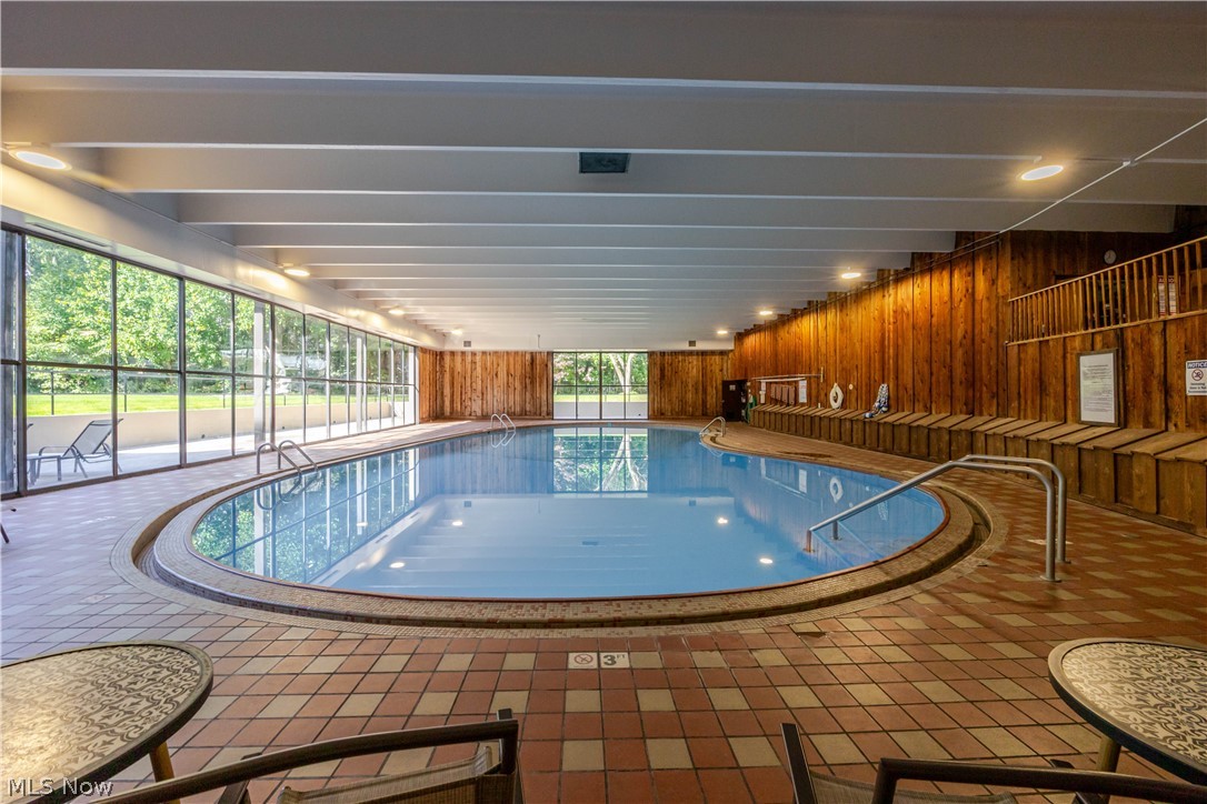 Indoor swimming pool with a curved tiled deck, floor-to-ceiling windows, and wood-paneled walls.