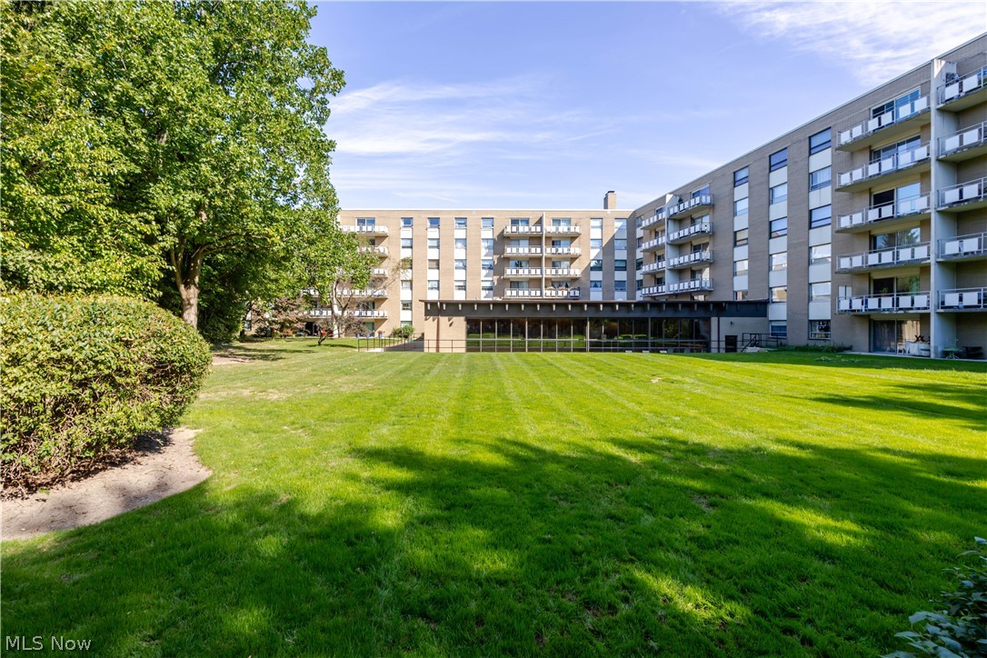 Condominium building overlooking a broad green lawn, with balconies and mature trees.