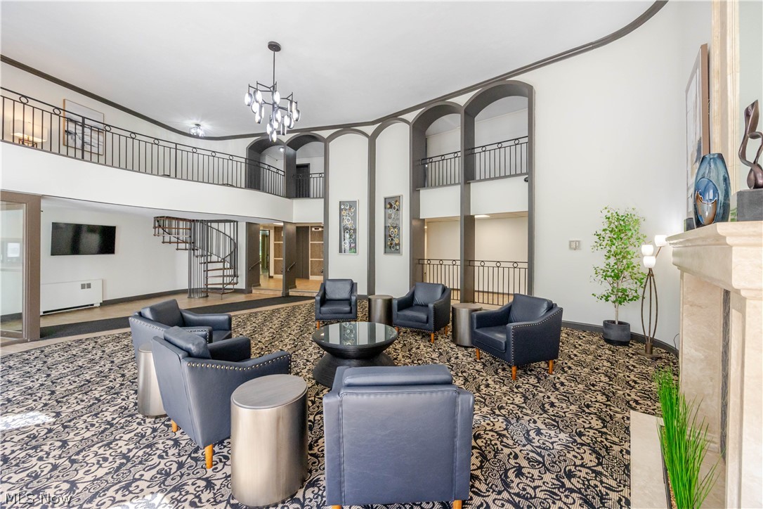 Furnished high-ceiling lobby with a curved staircase, upper gallery, and patterned carpet.