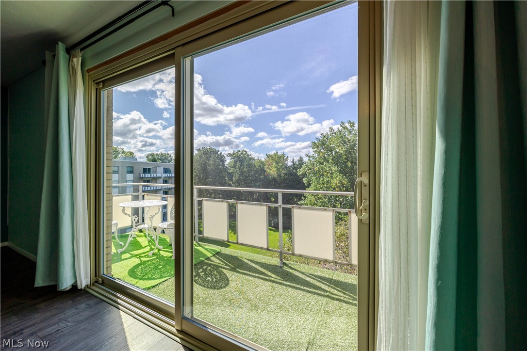 Sliding glass doors open onto a sunny balcony with outdoor seating and a leafy view.