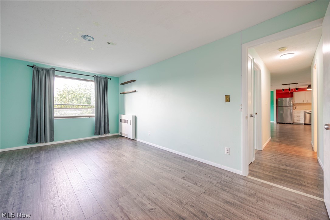 Empty room with gray plank flooring, teal walls, and a window beside the kitchen hallway.