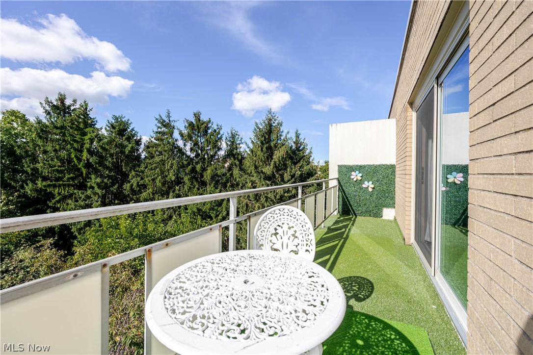 Balcony with white patio table and chairs, green turf, and views of trees.