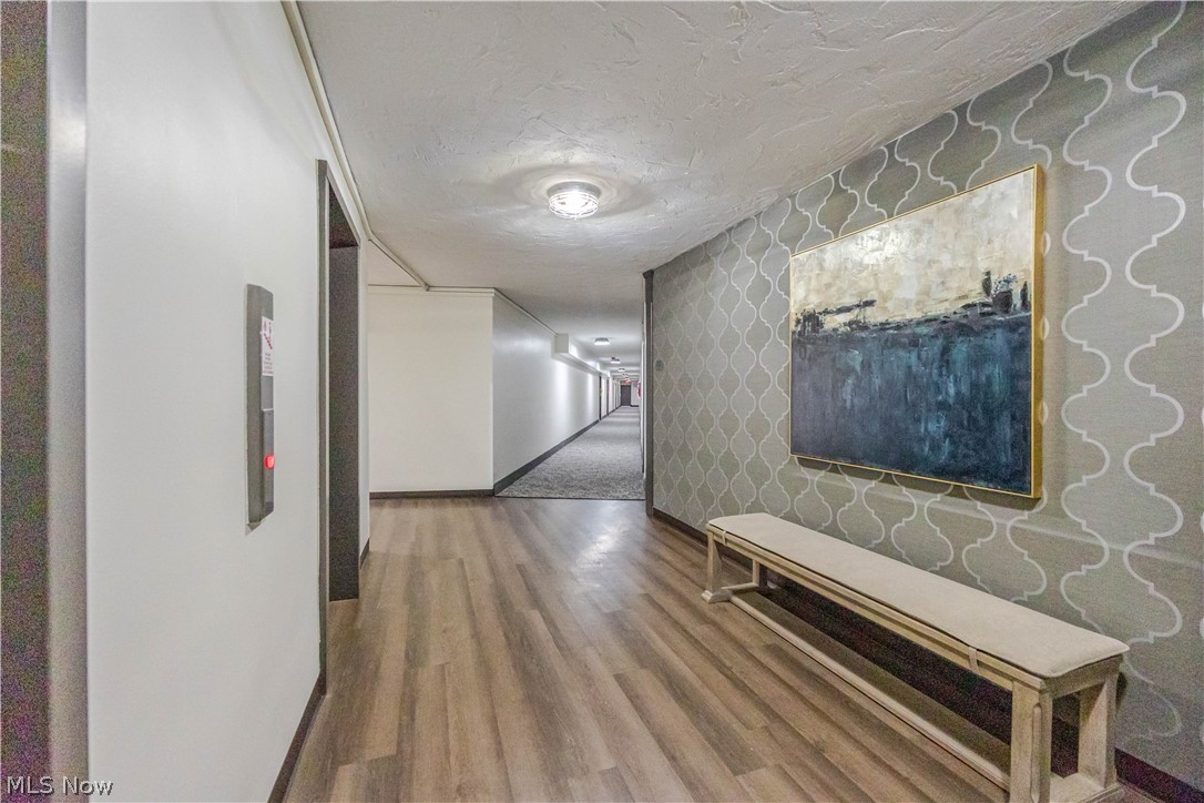 Building hallway with patterned wallpaper, a bench, and framed artwork beside an elevator call button.
