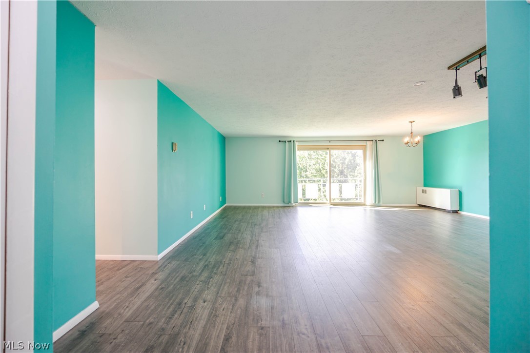 Vacant living room with teal walls, wood-look flooring, and sliding glass doors to a balcony.