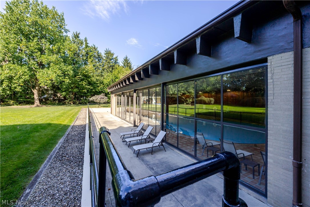 Condo patio with glass walls overlooking an indoor pool, furnished with lounge chairs beside a green lawn.