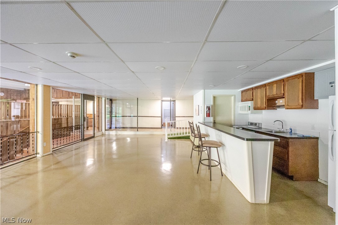 Open recreation room with a long kitchen counter, bar stools, and glass doors along one side.