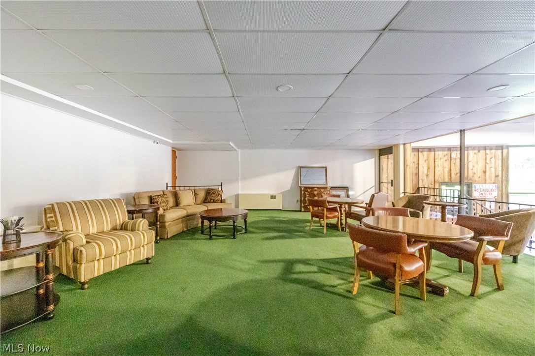 Furnished communal lounge with green carpet, striped sofa, and round dining tables.