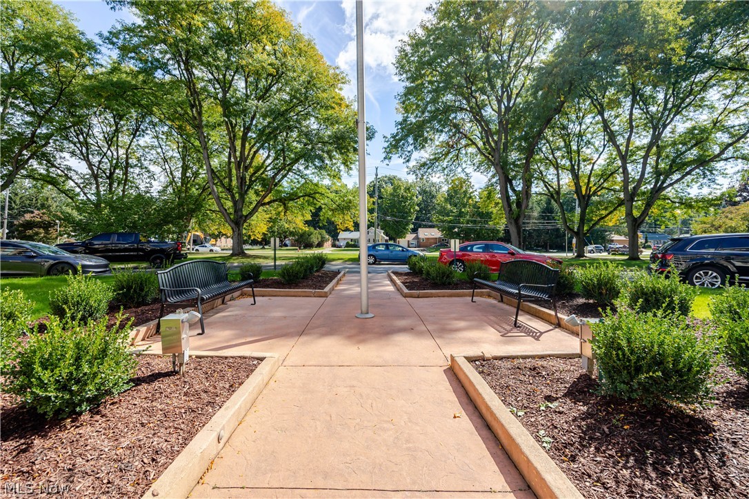 Landscaped walkway with benches and mature trees beside the road.