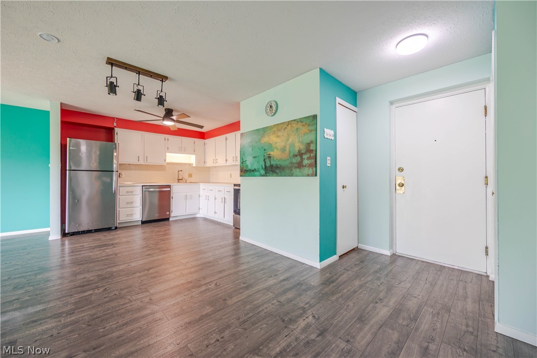 Open kitchen and entry with white cabinets, stainless steel appliances, and teal walls.