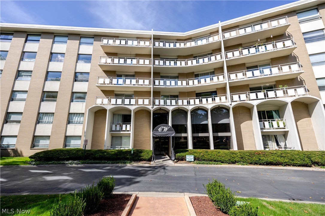 Condominium building with stacked balconies and an arched entrance beneath a clear blue sky.