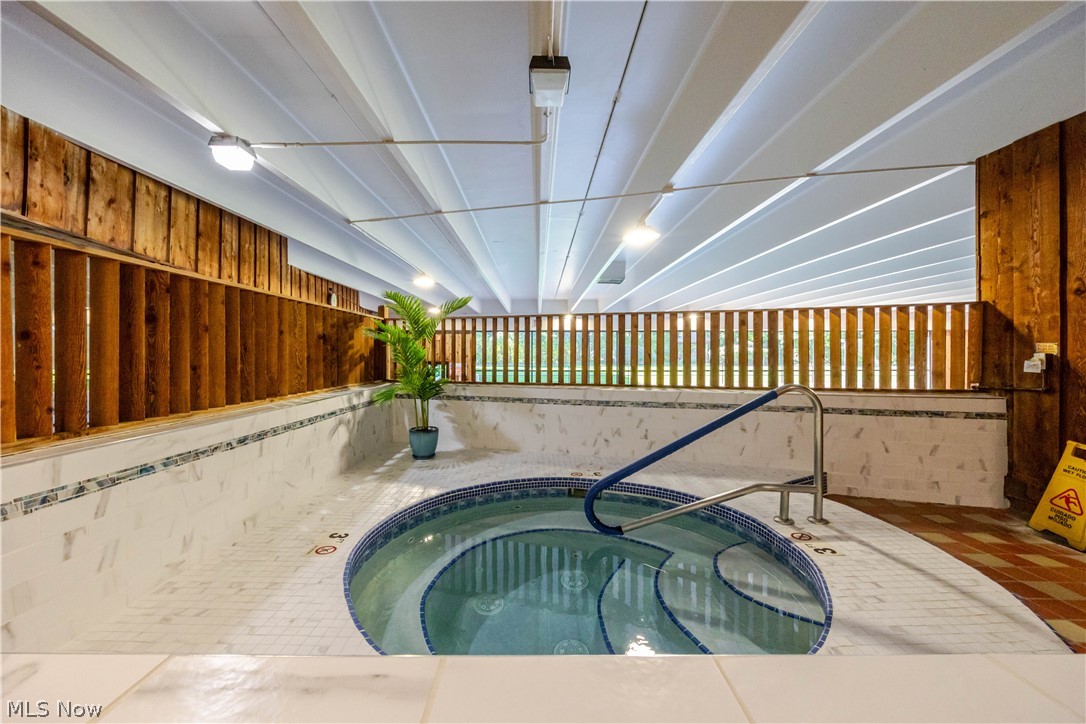 Indoor spa pool with tiled surround, metal handrails, and wood-slat walls.