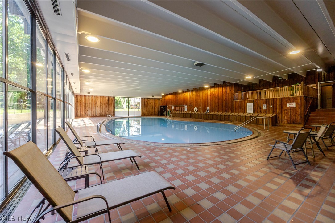 Indoor swimming pool with floor-to-ceiling windows, wood-paneled walls, and surrounding lounge chairs.