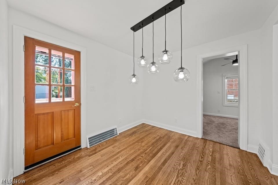 Empty dining room with hardwood floors, a multi-light pendant, and a wood-and-glass exterior door.