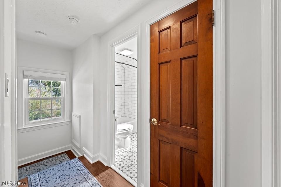 Bright hallway with a patterned rug and open wood door showing a tiled bathroom.