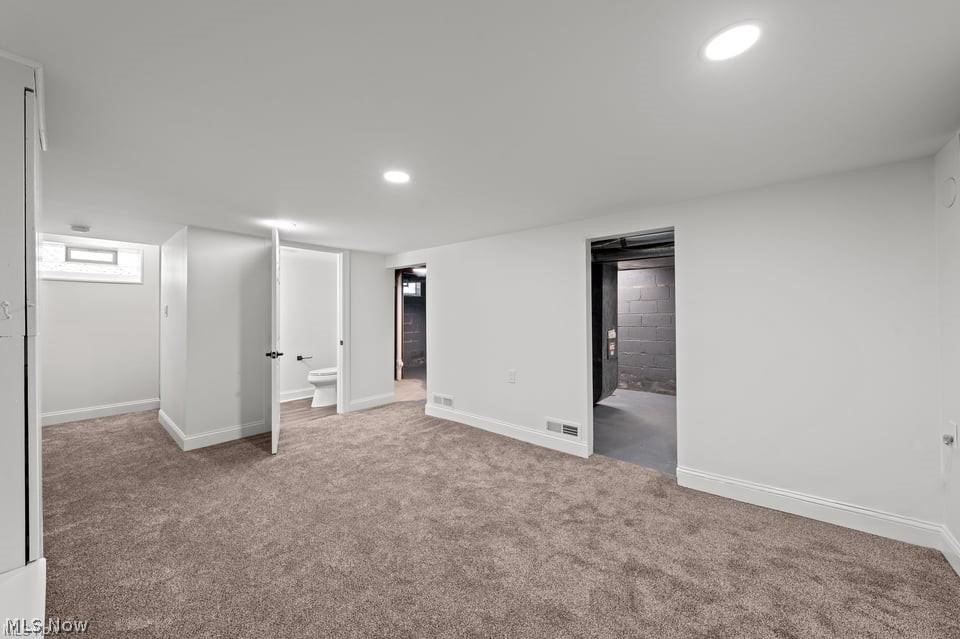 Finished basement room with beige carpeting and doorways to a bathroom and unfinished area.
