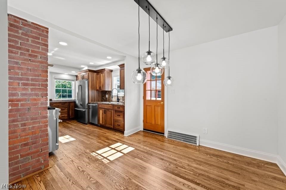 Kitchen with wood cabinetry, stainless steel appliances, pendant lights, and hardwood floors.