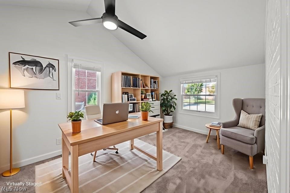 Home office with a wood desk and laptop, bookcase, gray armchair, and white brick wall.
