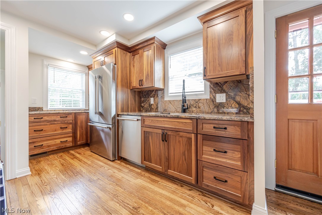 Kitchen with warm wood cabinetry, hardwood floors, stainless steel appliances, and a stone-pattern backsplash.