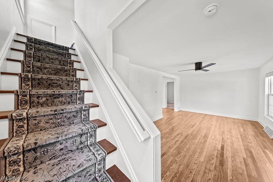 Carpeted staircase beside a bright, empty room with hardwood floors and a ceiling fan.