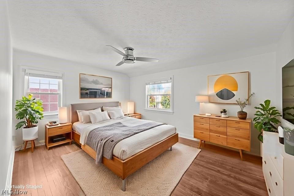 Virtually staged bedroom with a wooden bed, matching dressers, potted plants, and a ceiling fan.