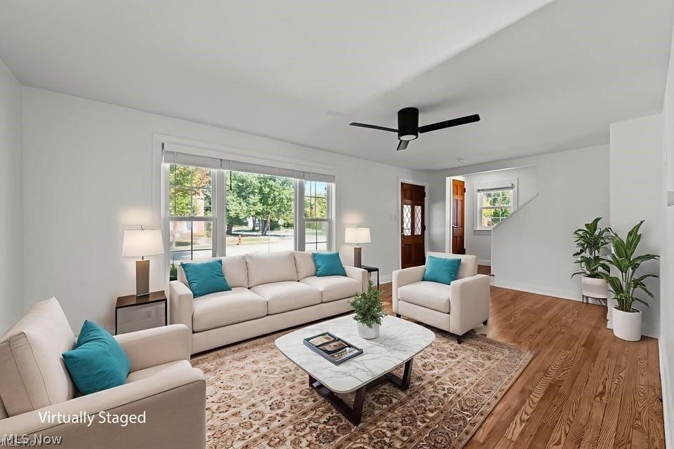 Virtually staged living room with white seating, teal pillows, a patterned rug, and a large front window.