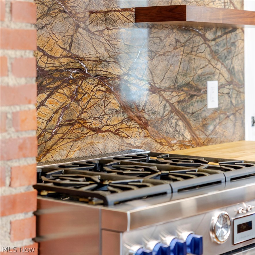 Kitchen gas range with blue knobs beneath a dramatic veined stone backsplash.