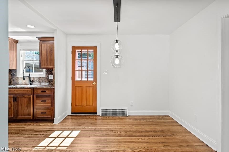 Vacant dining area with hardwood floors, pendant lights, and a wood-framed door beside the kitchen.