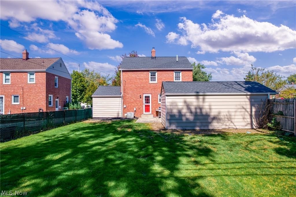 Rear of a red brick house with a red door, detached garage, and broad grassy backyard.