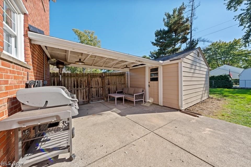Covered patio with outdoor seating and a grill beside a brick house and fenced yard.