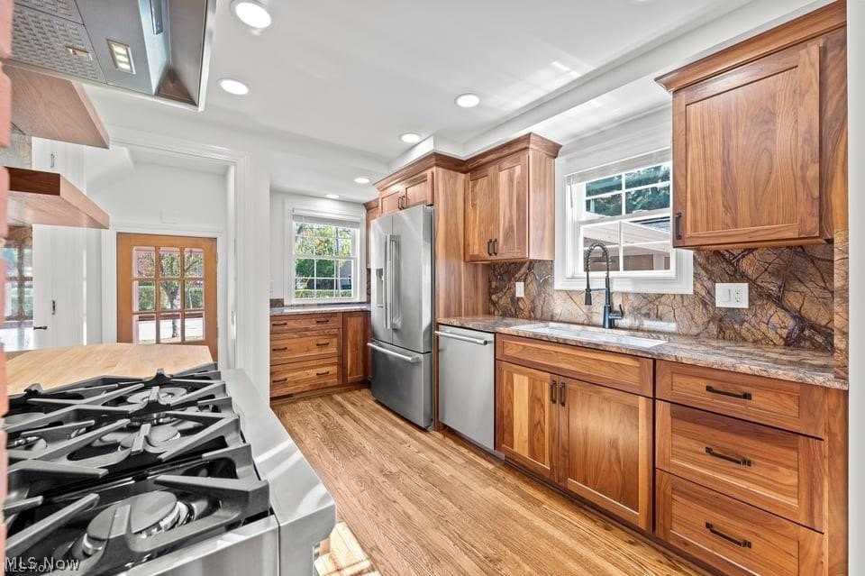 Kitchen with warm wood cabinets, stone backsplash, stainless steel appliances, and a prominent gas range.