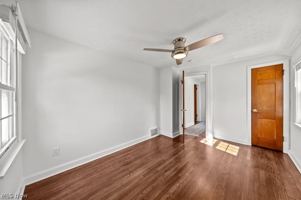 Vacant room with hardwood floors, tall windows, and a ceiling fan.