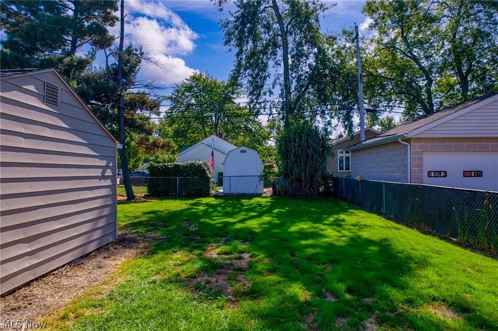 Backyard lawn with mature trees, chain-link fencing, and a detached white shed.