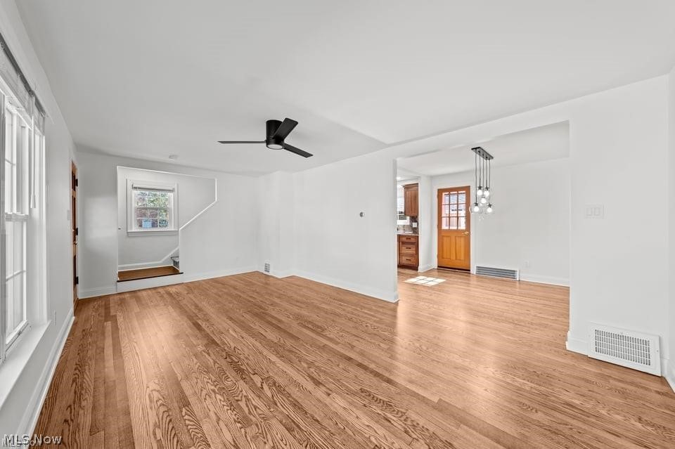 Empty living area with hardwood floors, large windows, and an opening to the kitchen and entry.