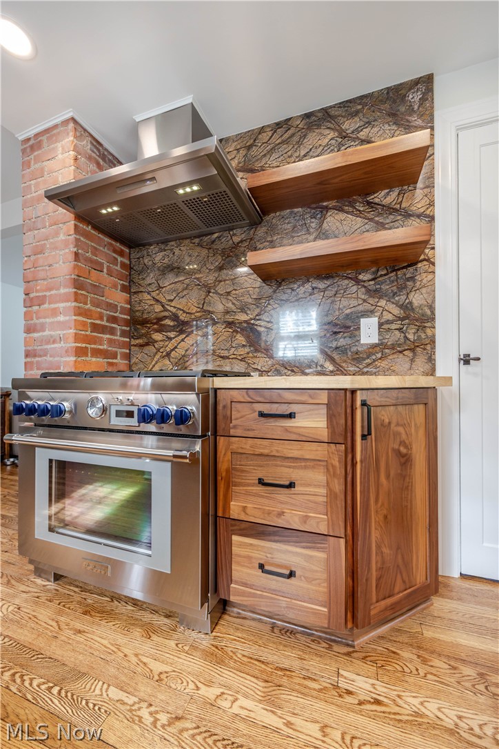 Kitchen range with blue knobs, walnut cabinetry, wood shelves, and a dramatic patterned stone backsplash.
