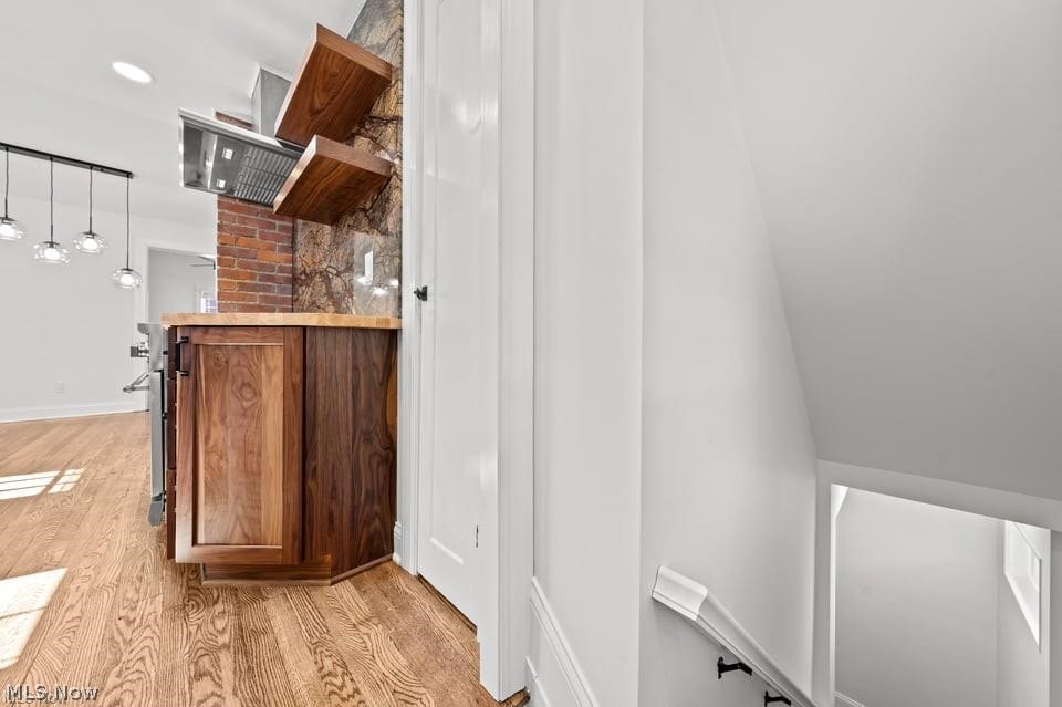 Kitchen with a wood-paneled island, brick and stone backsplash, and hardwood floors, viewed from beside the stairwell.