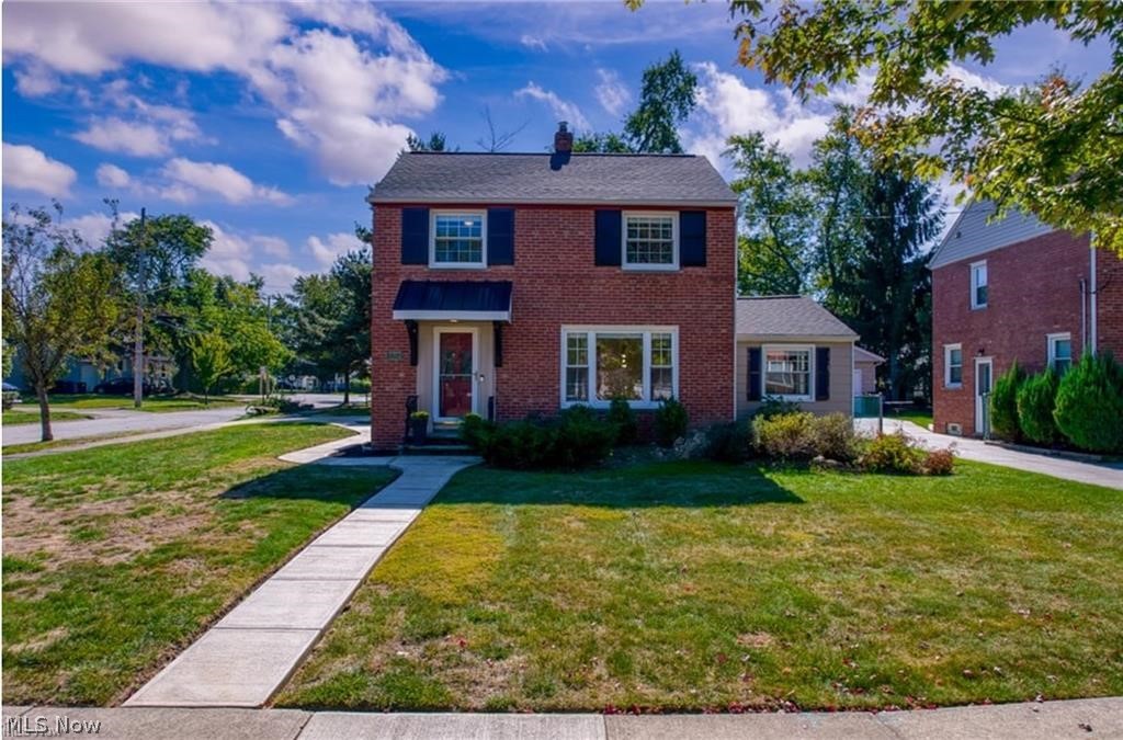 Two-story red brick house with dark shutters and a walkway across the front lawn.