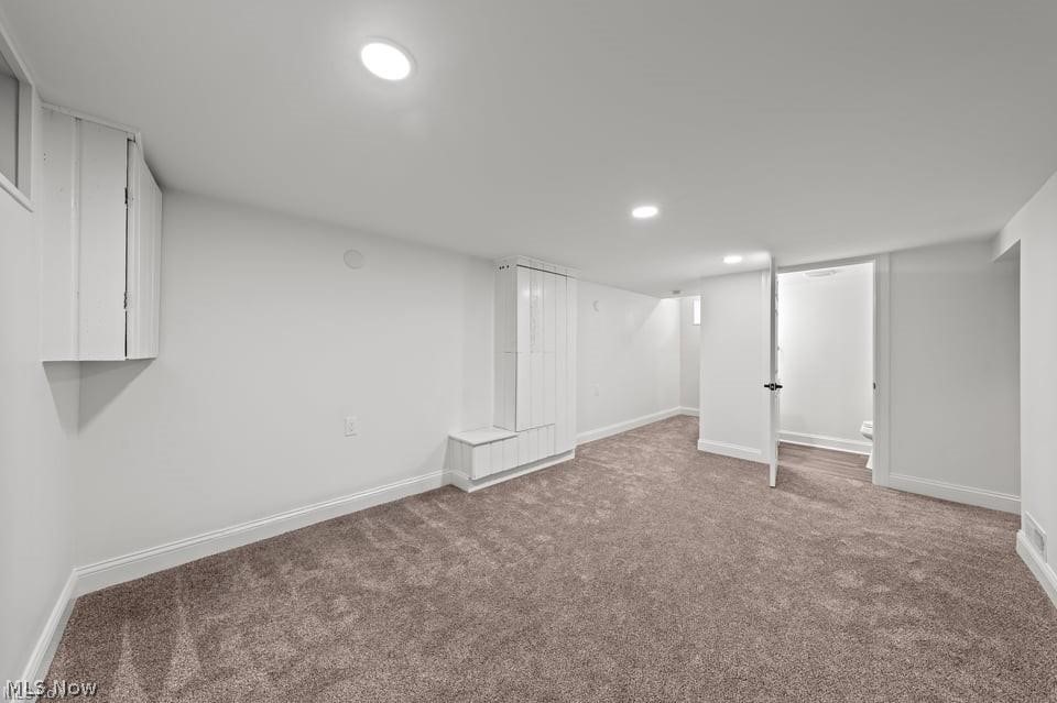 Finished basement room with taupe carpet, built-in white cabinets, and an open bathroom doorway.