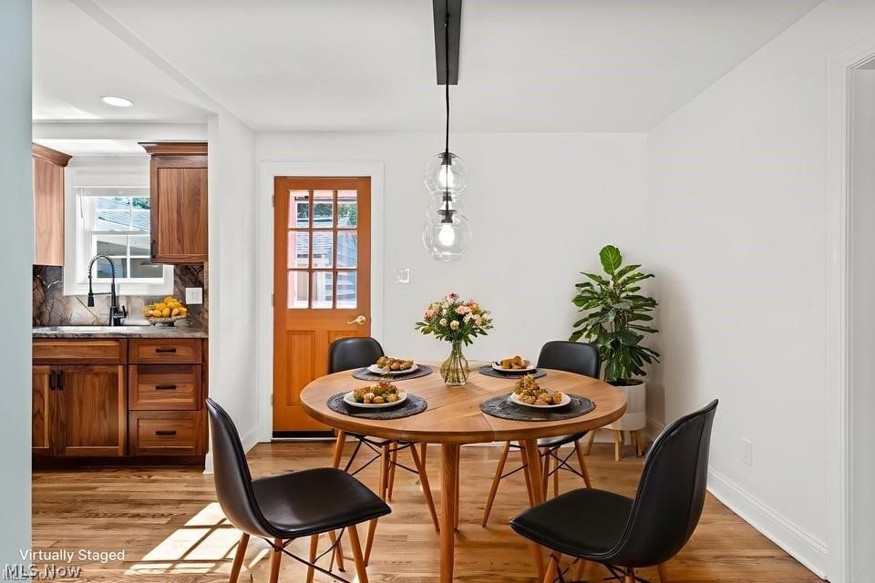 Dining room with a set round wooden table, black chairs, pendant lights, and adjoining wood-cabinet kitchen.
