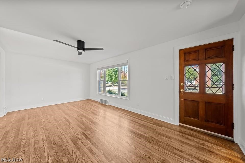 Vacant room with light hardwood floors, a black ceiling fan, and a dark wood front door with decorative glass.