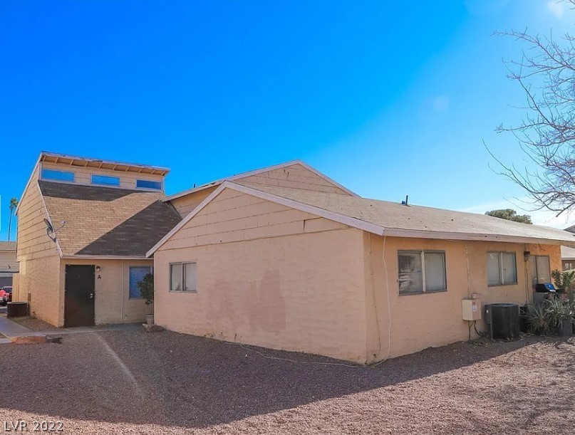 Tan stucco home's exterior with gravel yard, recessed entry, and bare tree under a clear sky.