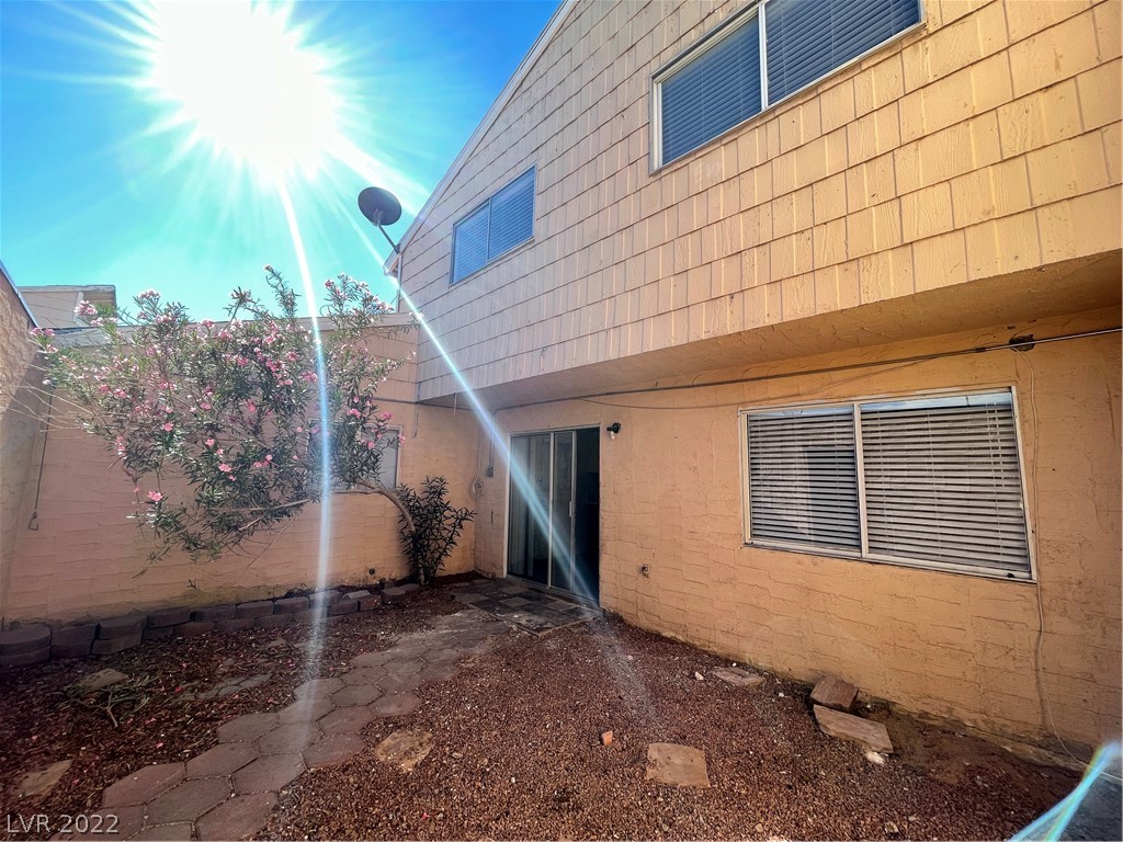 Rear courtyard patio with flowering shrubs, gravel landscaping, and a two-story tan residence.