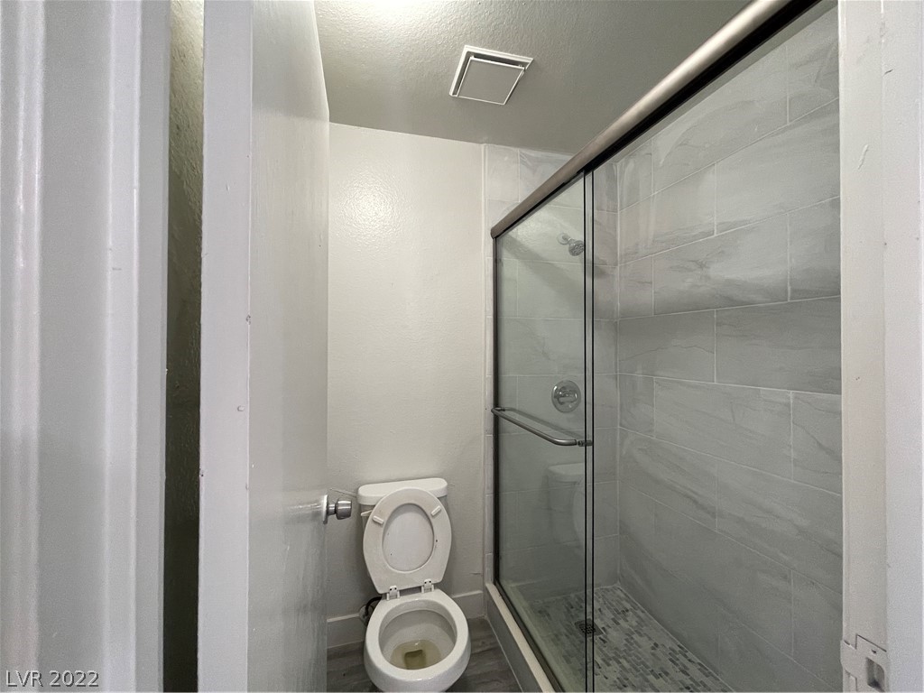 Bathroom with a glass-enclosed, gray-tiled shower beside a toilet.