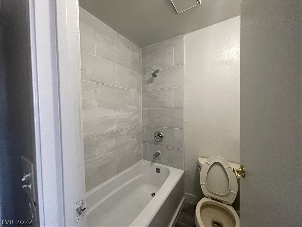 Bathroom with a white bathtub, large gray tile surround, and toilet beside the tub.