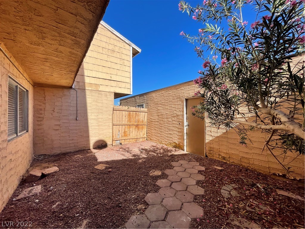Enclosed townhouse courtyard with a paver path, wooden gate, and flowering tree.