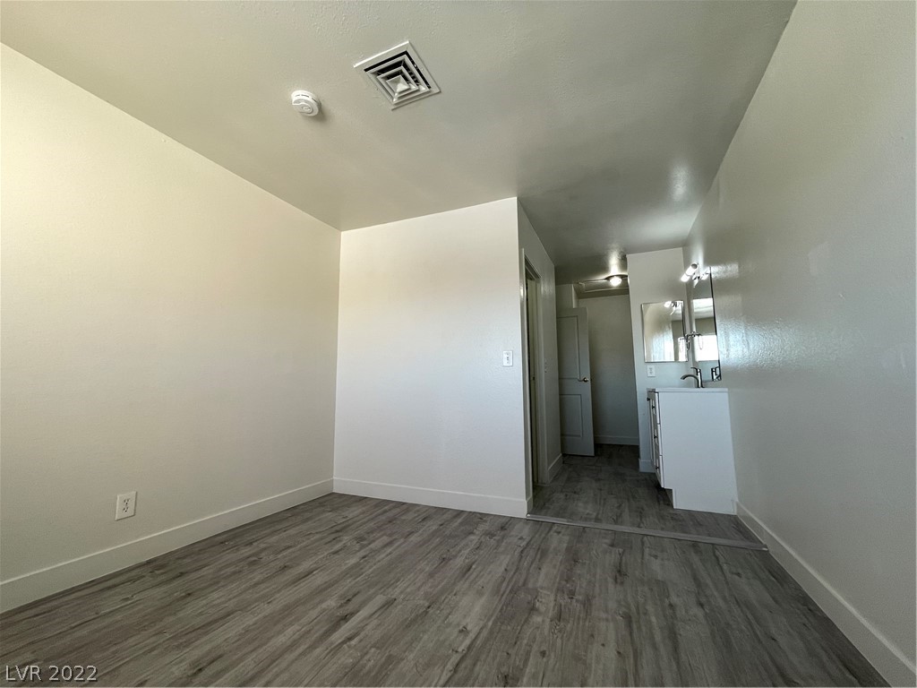 Vacant room with gray wood-look floors opening to a bathroom vanity.