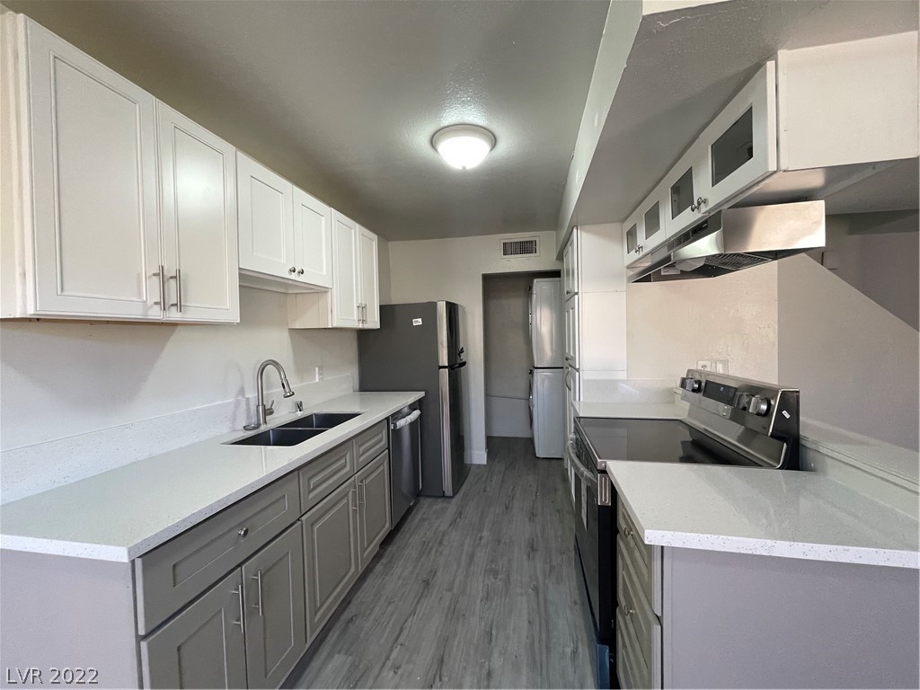 Galley kitchen with white cabinets, gray lower cabinets, stainless-steel appliances, and gray plank flooring.